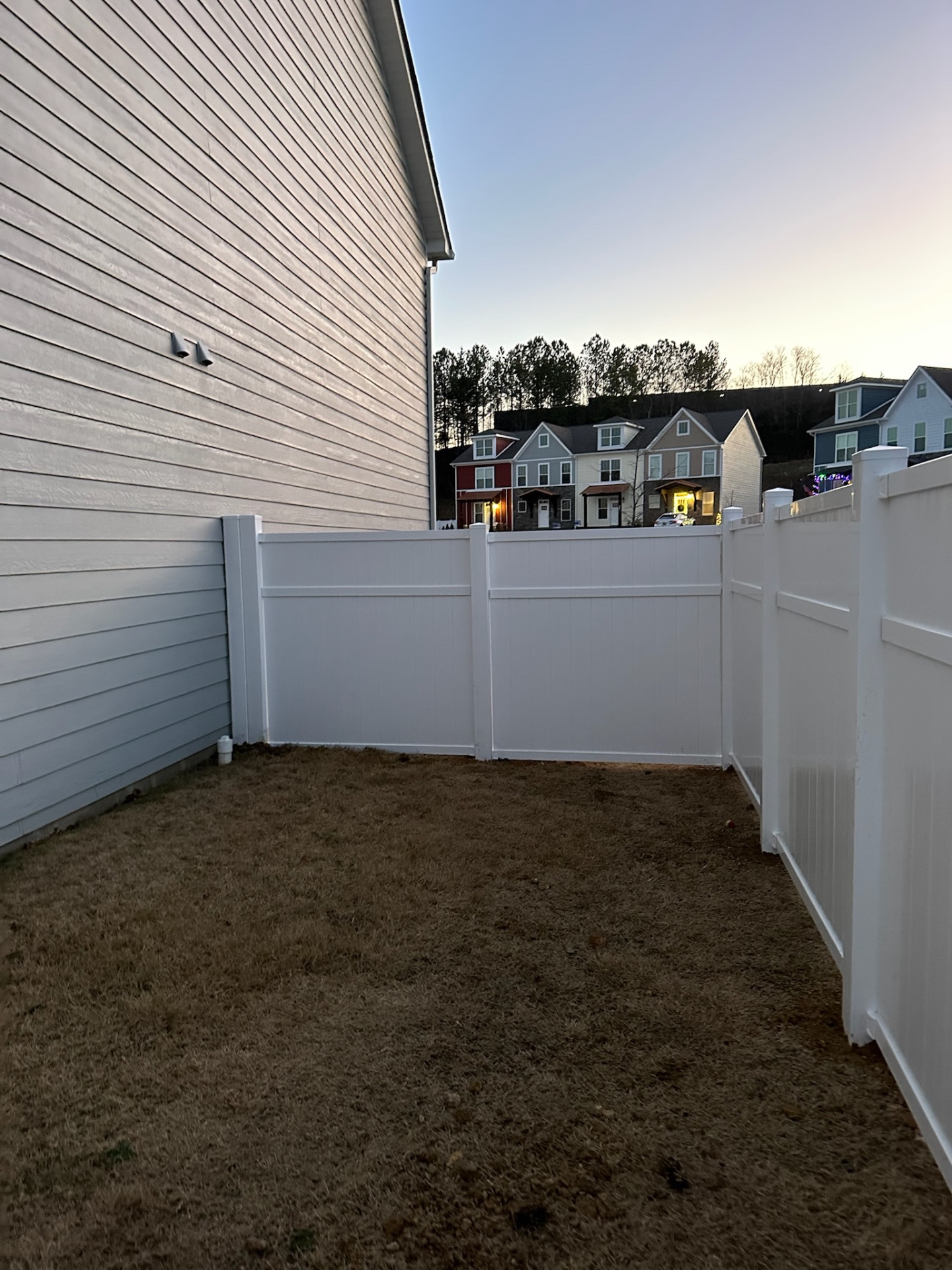 White vinyl privacy fence running along a house at dusk