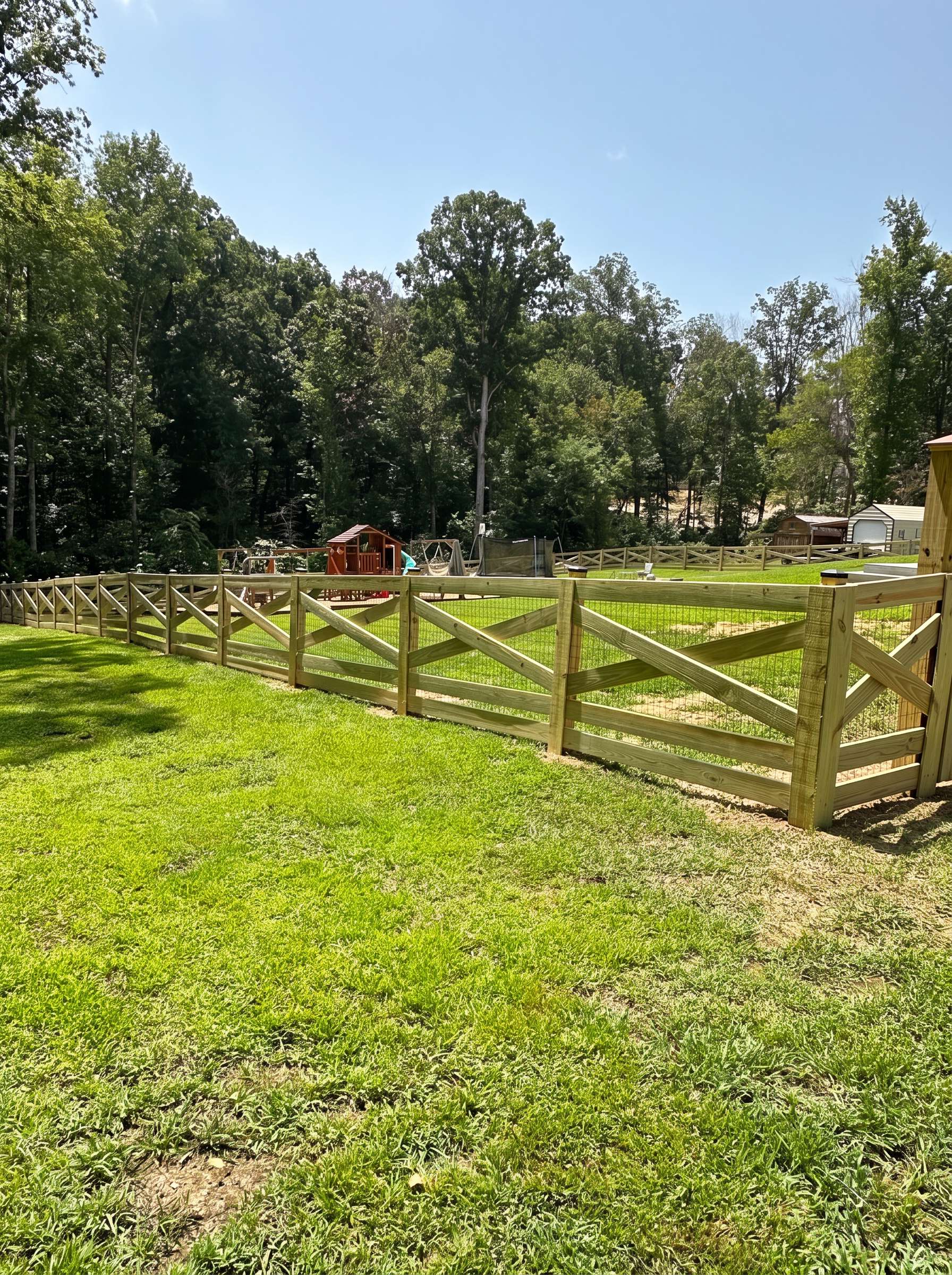 X-brace wood fence with wire backing around a backyard playground