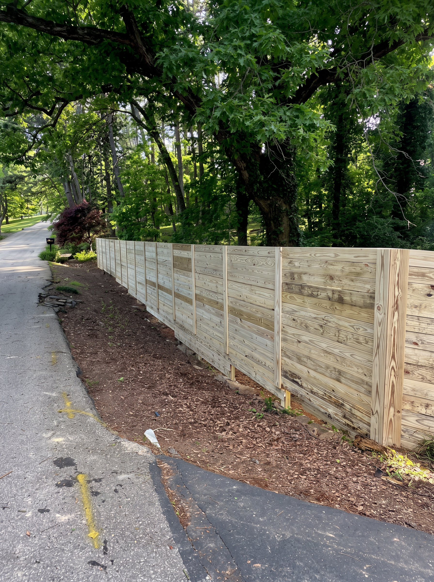 Long horizontal board wood fence following a shaded country road