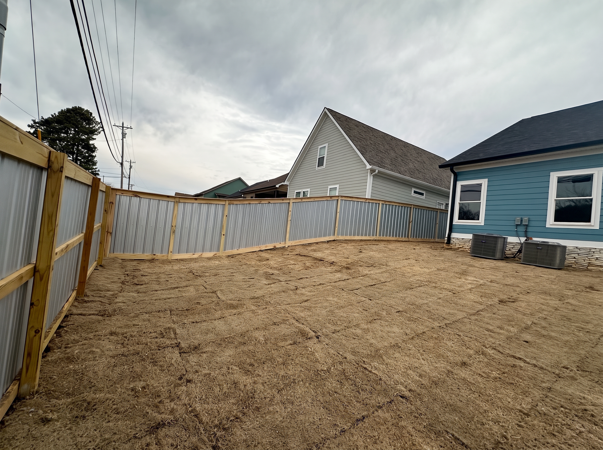 Corrugated aluminum privacy fence with wood framing wrapping a backyard beside a blue house