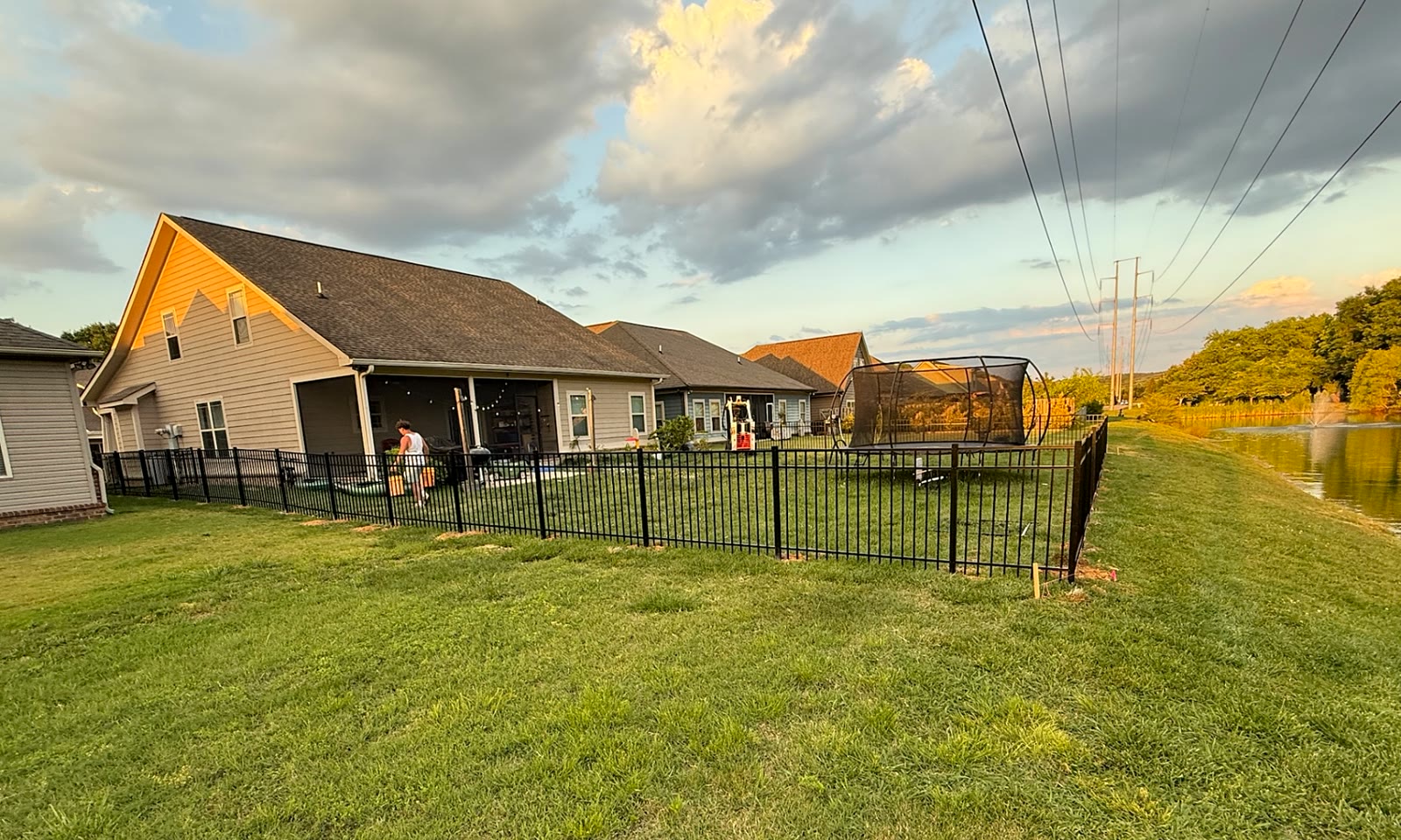 Black aluminum backyard enclosure beside a pond at sunset