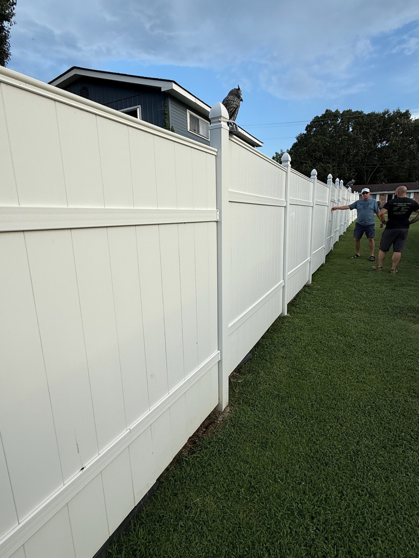 Long white vinyl privacy fence with pyramid post caps along a lawn