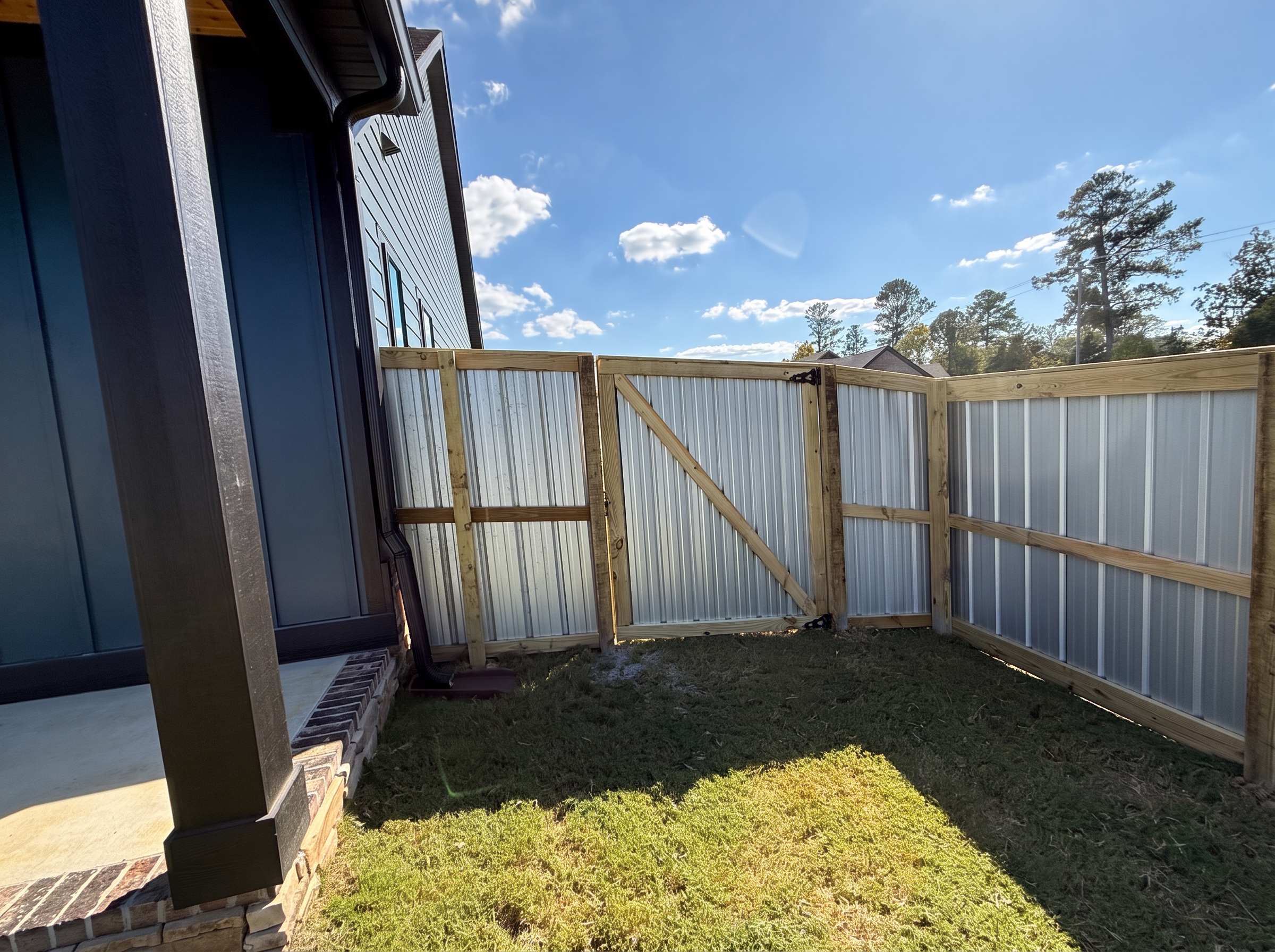 Wood-framed corrugated aluminum walk gate with diagonal bracing and black hinges beside a porch