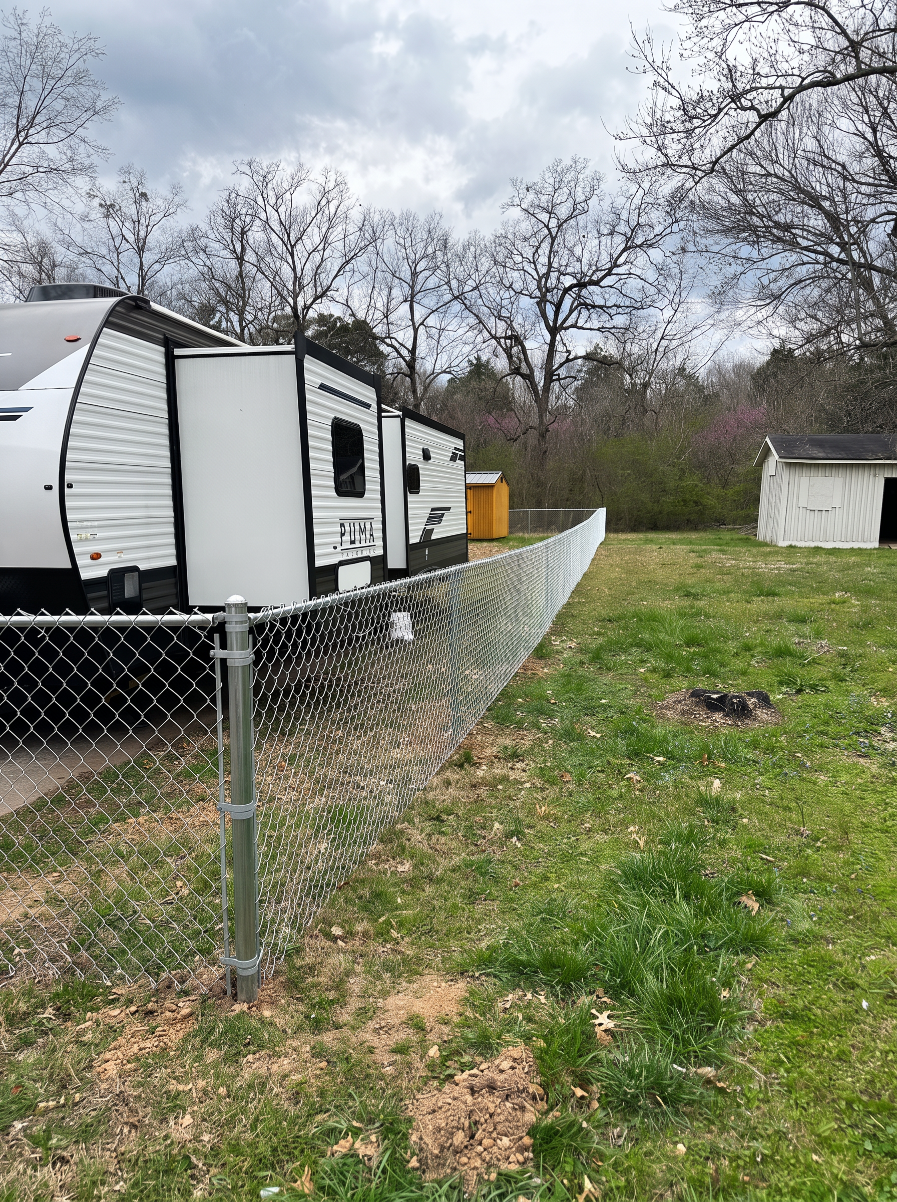 Galvanized chain-link fence beside a travel trailer and backyard sheds