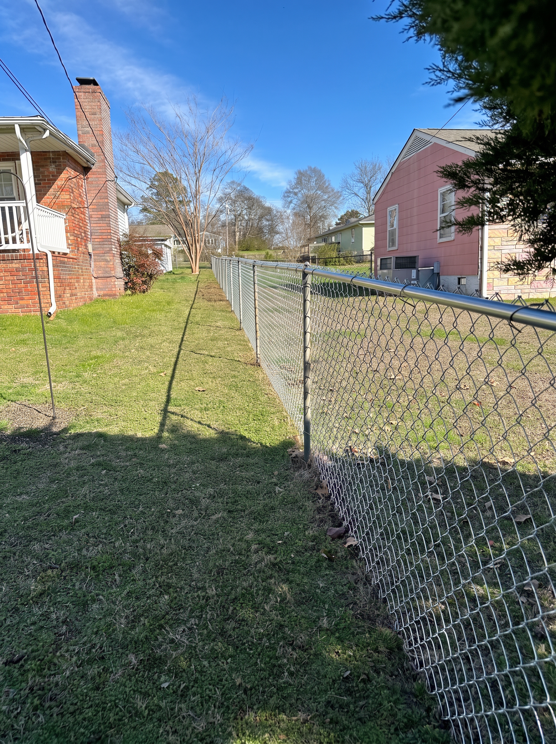 Galvanized chain-link fence running between a brick home and a pink house