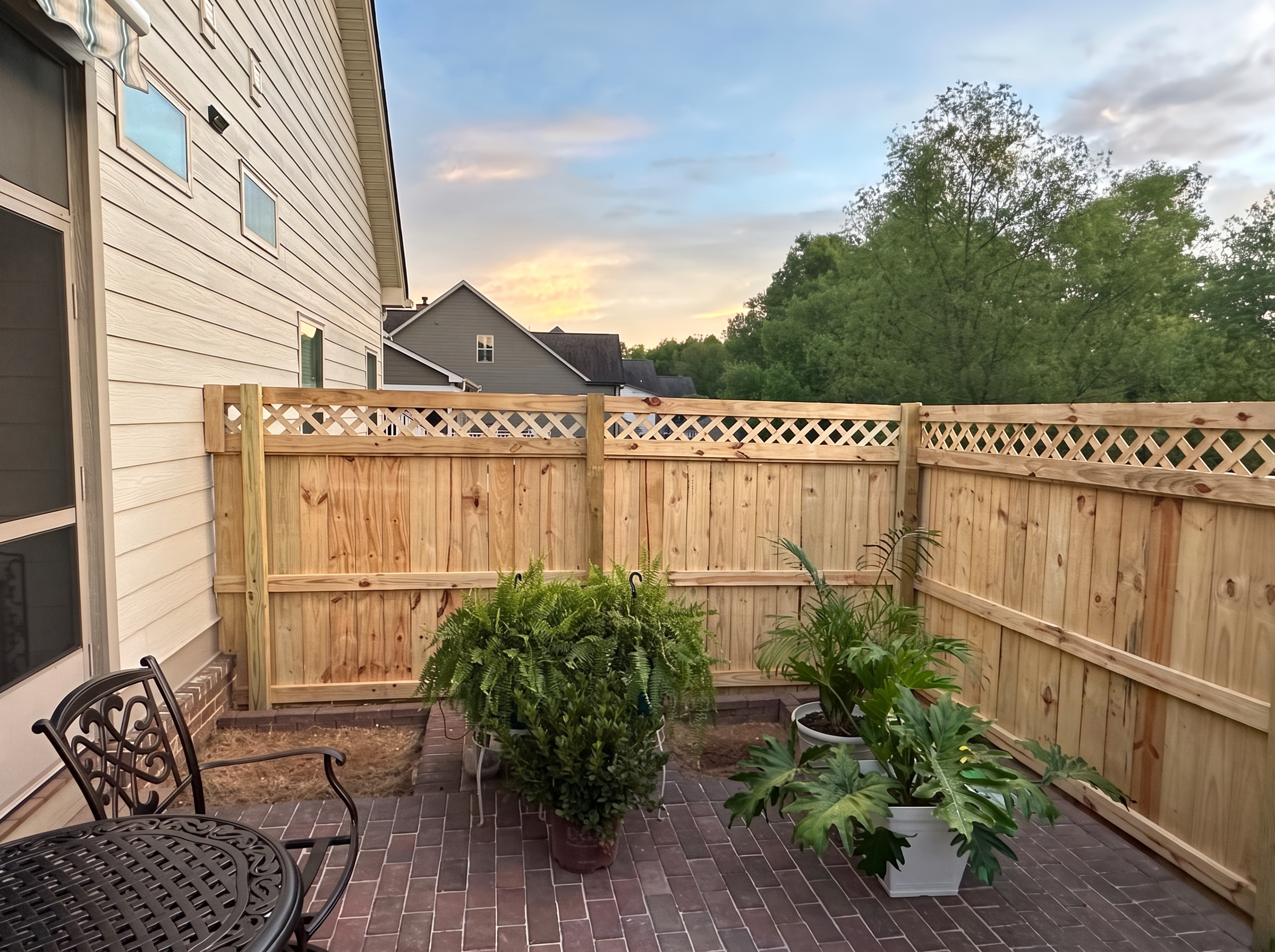 Lattice-top wood privacy fence enclosing a brick patio at sunset