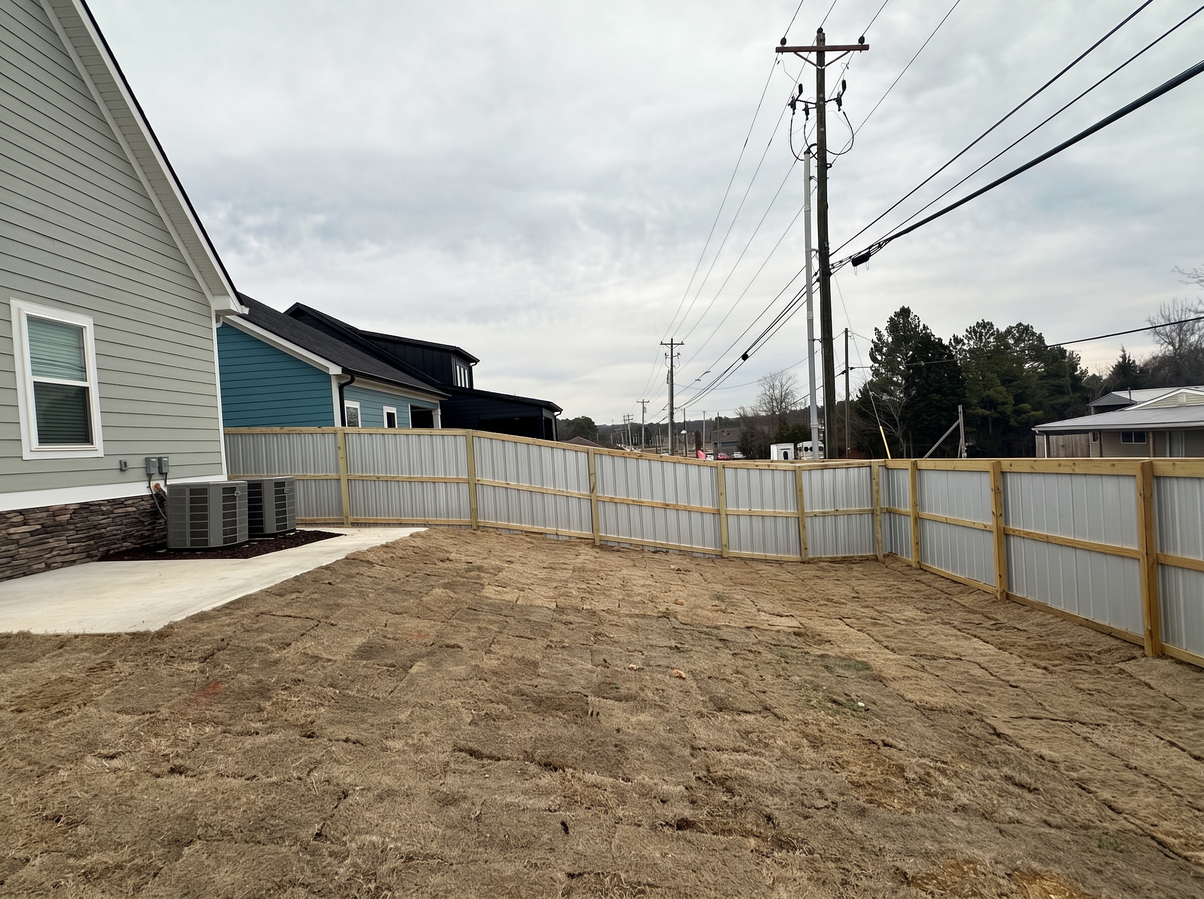 Interior view of corrugated aluminum fence with wood posts and horizontal rails enclosing a yard
