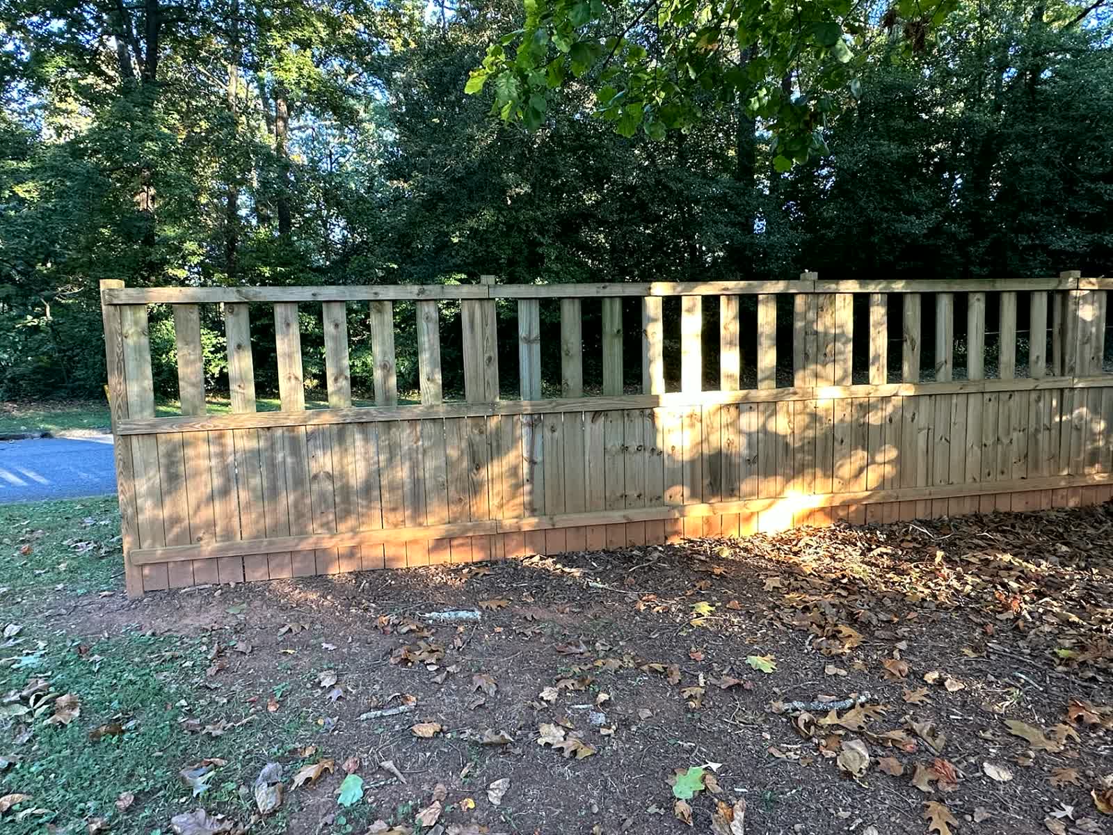 Wood privacy fence with a picket accent rail along a tree line