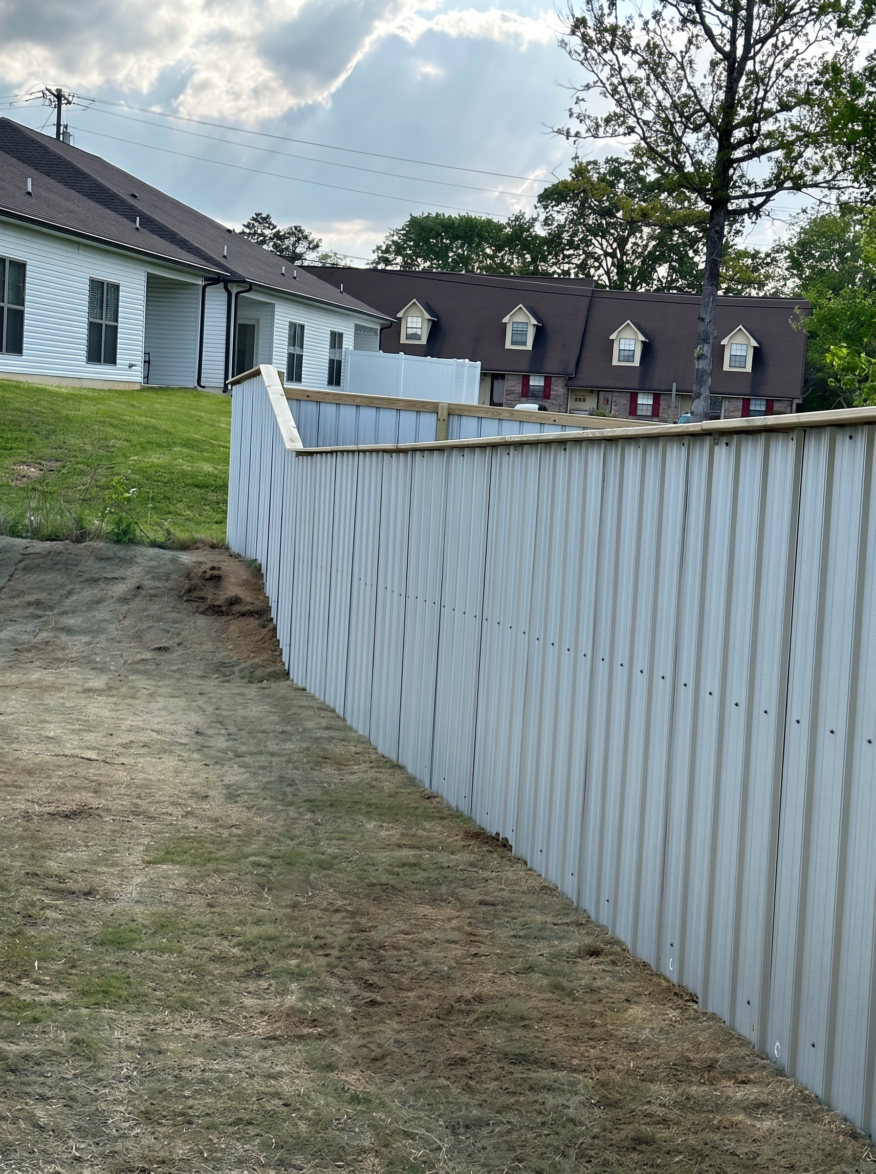 Corrugated aluminum privacy fence with a wood cap turning a residential yard corner