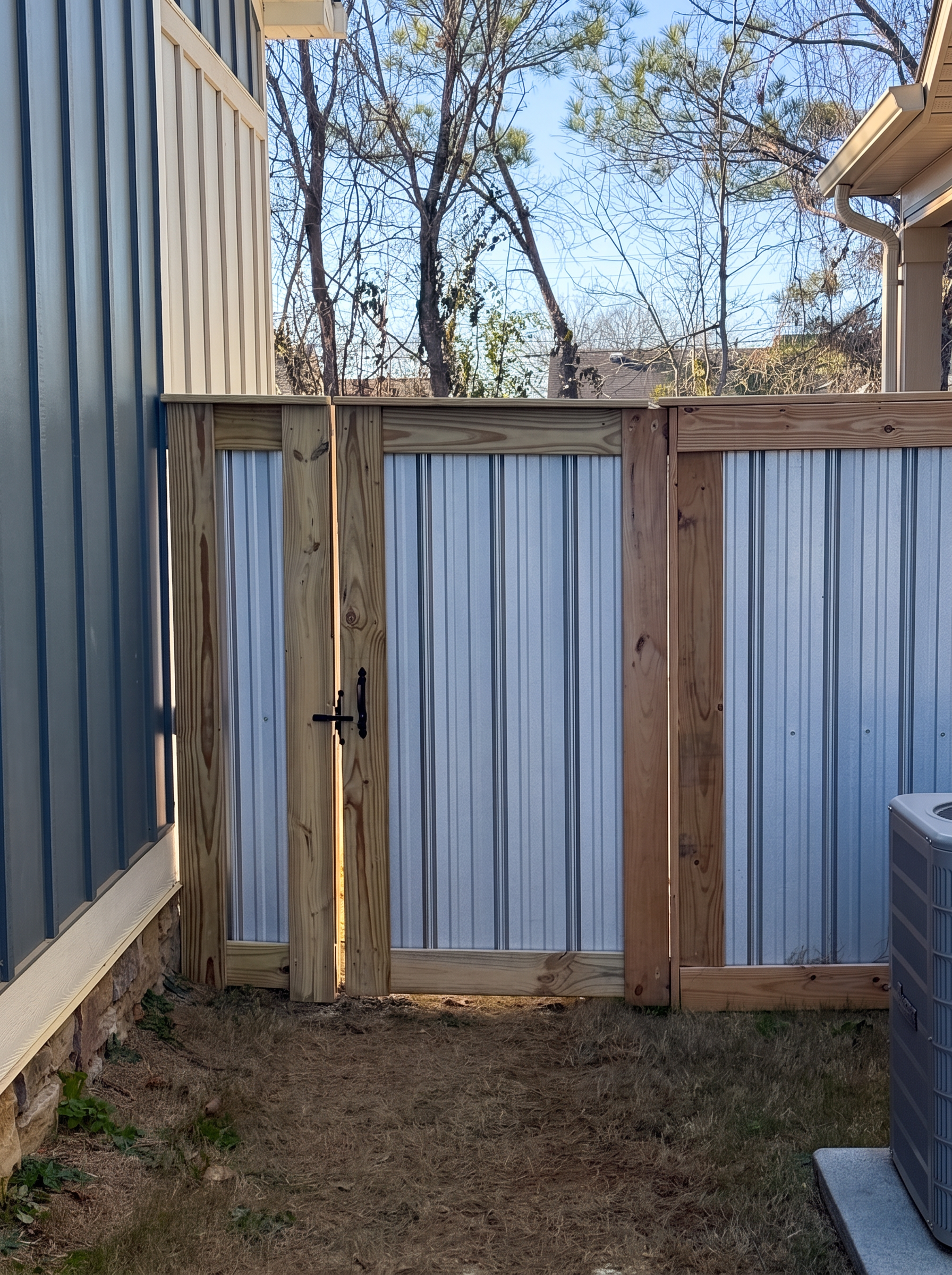 Corrugated aluminum walk gate with wood framing and black latch hardware between houses