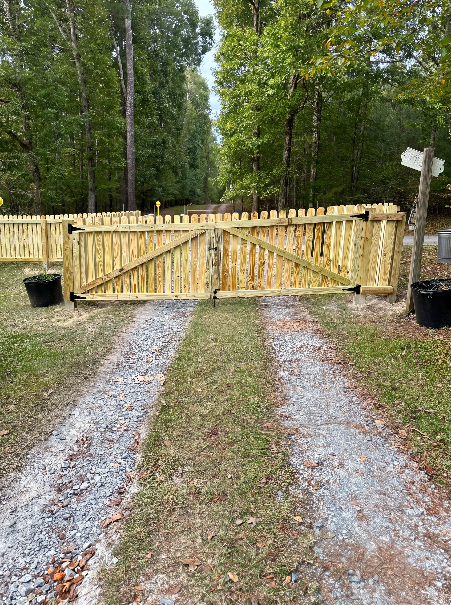 Double wood picket gate with diagonal bracing across a gravel driveway