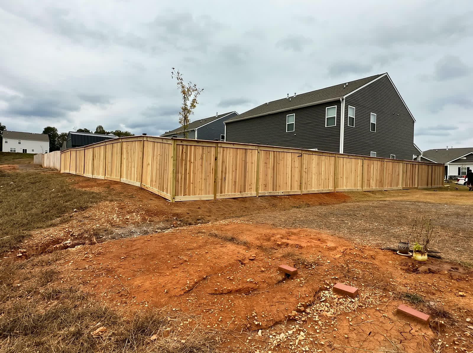 Cedar board-on-board privacy fence stepping across a graded new-construction lot