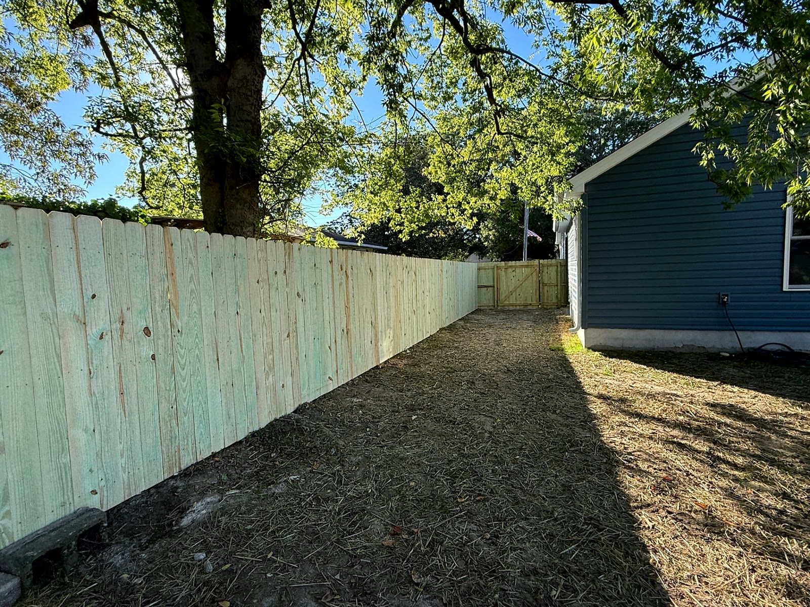 Long wood privacy fence under shade trees leading to a double gate