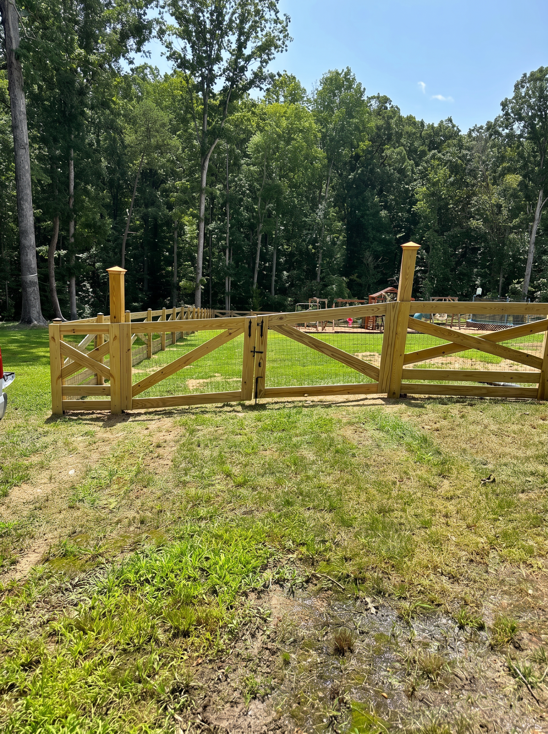 X-brace wood double gate with wire mesh on a sloped lawn